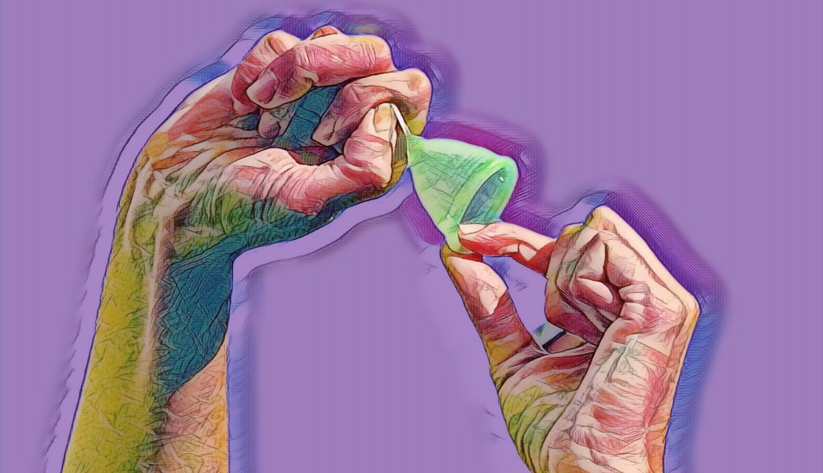 2 handen in de lucht met een groene menstruatiecup. de linkerhand houdt de bovenkant van de cup vast terwijl de rechterhand de cup hard aan het steeltje omhoog trekt